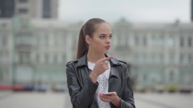 Boş şehir gquere arka planda sabahın erken saatlerinde ayakta güzel mutlu kız portresi. Sevimli kız bir harita üzerinde bir rota kontrol ederken bir cep telefonu içine bakar. Gerçek insanlar serisi.