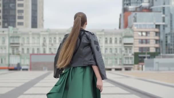 멋진 저녁 녹색 드레스에 아름다운 화려한 소녀는 마천루 근처 빈 도시 광장에 쾌활하고 행복 산책. — 비디오