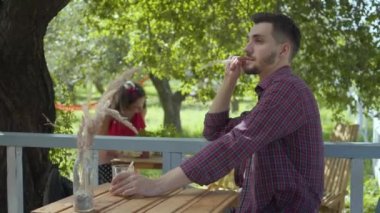 Genç sakallı adam arka planda tencere çiçek dikim retro giysiler içinde çekici kız konsantre ederken ön planda çay içme. Rutin bir hayat. Karısı çalışırken koca rahatlatıcı