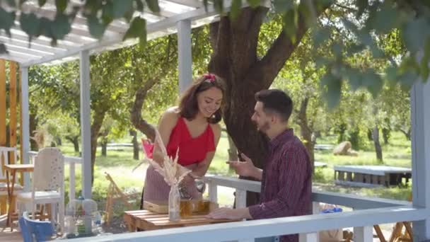 Joven camarera en blusa retro y falda sirviendo té caliente a su cliente que se sienta a la mesa sonriendo y coqueteando. Café de estilo vintage — Vídeo de stock