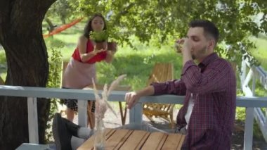 Sakallı adam arka planda tencere çiçek dikim retro giysiler içinde çekici kız konsantre ederken ön planda çay içme. Rutin bir hayat. Karısı çalışırken koca rahatlatıcı