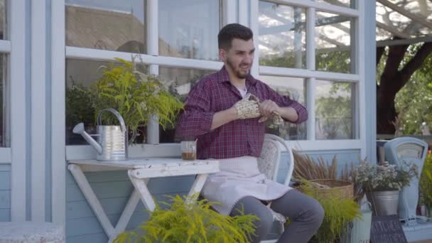 피곤한 젊은 전문 농부는 정원 장갑을 벗고 마을 집에 앉아 차를 마시고. 남자는 정원에서 작업 후 휴식. 농촌 생활. — 비디오
