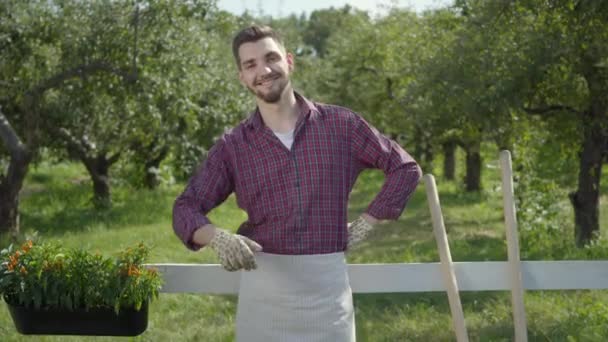 Agricultor confiante mostrando polegares de pé no jardim de verão verde perto da cerca. O homem que descansa depois do trabalho a olhar para a câmara. Estilo de vida rural, jardinagem. Série de pessoas reais . — Vídeo de Stock