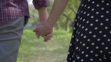 Bahçede el ele yürüyen genç pozitif çiftin yakın çekim. Mutlu erkek ve kadın dışarıda vakit geçiriyorlar. Doğayla bağlantı, kırsal yaşam, romantik buluşma. Geri görünüm