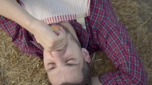 Jeune homme barbu allongé sur le foin mangeant des pommes fraîches. Le fermier se repose après le travail. Style de vie rural, style champêtre . — Video