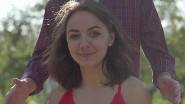 Portrait de femme séduisante regardant la caméra sourire tandis que l'homme barbu venant de derrière et couvrant ses yeux avec les mains. Rendez-vous romantique en plein air, mode de vie rural — Video