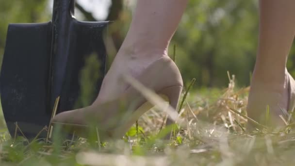 Pies de cerca de la señora de la moda en zapatos beige en los tacones altos de pie en la hierba cerca de la pala. Habitante de la ciudad en el pueblo. Vida en el campo — Vídeos de Stock