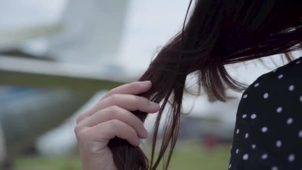 Close-up of female hand touching her dark hair in front of the blurred plane. Concept of traveling, aircraft, weekend. The happy woman traveling — Stock Video