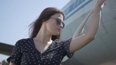 Elinde beyaz şal ile güneş gözlüğü genç esmer kız büyük uçağın önünde duran ve uzağa bakıyor. Yaz. Seyahat insebunu. Seyahat kavramı, uçak, hafta sonu