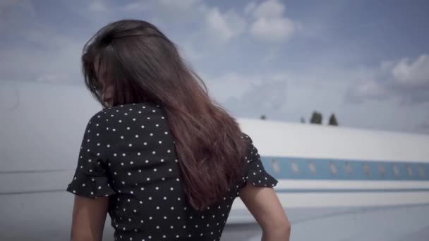 Glücklich junge brünette Mädchen posiert und blickt in die Kamera vor dem großen weißen Flugzeug, die Haare flattern im Wind. Sommerzeit. Reisefreude. Reisekonzept, Flugzeug, Wochenende — Stockvideo
