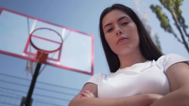 Ritratto giovanissima bruna ragazza guardando la macchina fotografica in piedi sul campo da basket all'aperto. Concetto di sport, potere, competizione, stile di vita attivo. Sport e tempo libero . — Video Stock