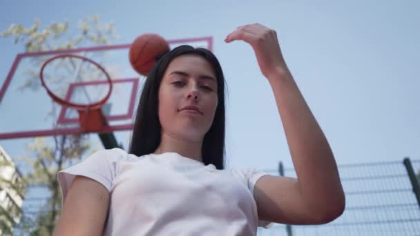 Retrato linda chica morena adolescente lanza una pelota de baloncesto en el ring mirando a la cámara de pie en la cancha de baloncesto al aire libre. Concepto de deporte, estilo de vida activo. Deportes y recreación . — Vídeos de Stock