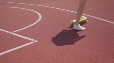 Beyaz spor ayakkabılı kadın bacaklarının yakın çekim kızı açık basketbol sahasında sarı kaykay sürüyor. Gölge kızı takip ediyor. Spor kavramı, rekabet, aktif yaşam tarzı. Spor ve rekreasyon.