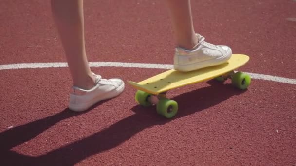 Pernas femininas em tênis brancos ao lado de um skate amarelo em uma quadra de basquete ao ar livre. Conceito de esporte, competição, estilo de vida ativo. Esportes e recreação . — Vídeo de Stock