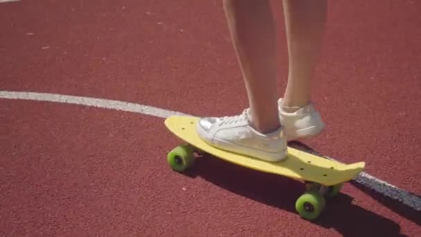 Närbild kvinnliga ben i vita sneakers flicka ridning gul skateboard på en utomhus basketplan. Begreppet idrott, konkurrens, aktiv livsstil. Sport och fritid. — Stockvideo
