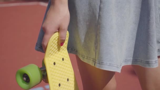 화창한 날씨에 야외에서 서있는 동안 인식 할 수없는 소녀는 그녀의 손에 노란색 스케테를 들고. — 비디오