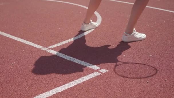Τα πόδια της γυναίκας με άσπρα παπούτσια κάνουν προθέρμανση πριν παίξουν τένις στο γήπεδο. Η σκιά επαναλαμβάνει την κίνηση για το κορίτσι. Έννοια του αθλητισμού, δύναμη, ανταγωνισμός, ενεργός τρόπος ζωής — Αρχείο Βίντεο