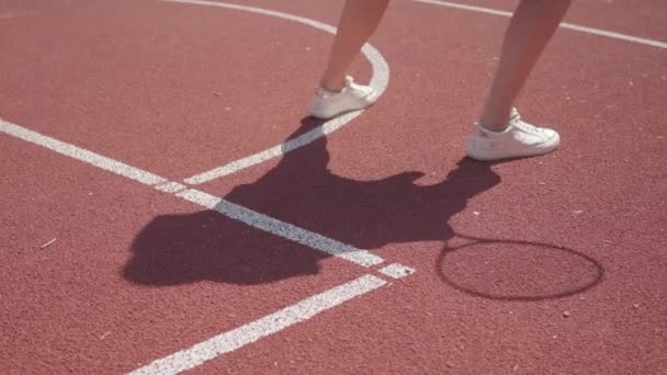 Beine einer Frau in weißen Turnschuhen beim Aufwärmen, bevor sie auf dem Platz Tennis spielt. Schatten wiederholt die Bewegung des Mädchens. Konzept von Sport, Power, Wettbewerb, aktivem Lebensstil — Stockvideo