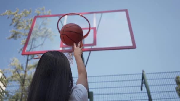 Achteraanzicht van brunette vrouw zonder succes het gooien van de bal in de mand. Concept van sport, macht, competitie, actieve levensstijl. Het meisje leren om basketbal te spelen op het Hof. Slow Motion. — Stockvideo