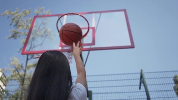 Vista posterior de la mujer morena sin éxito lanzando la pelota en la canasta. Concepto de deporte, poder, competencia, estilo de vida activo. La chica aprendiendo a jugar baloncesto en la cancha. Movimiento lento . — Vídeos de Stock