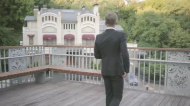 Terasta yürüyen genç ve iyi giyimli bir işadamının arka görünümü. Ofis yöneticisi doğaya hayran açık havada dinlendirici. Mola süresi, konforlu işyeri.