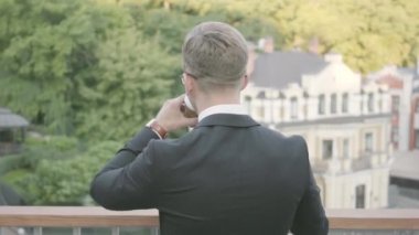 Terasta kahve içen genç hırslı başarılı işadamının geri görünümü. Ofis yöneticisi doğaya hayran açık havada dinlendirici. Mola süresi, konforlu işyeri, serbest.