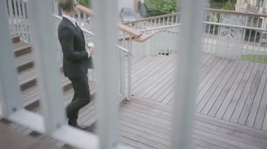 Genç başarılı işadamı netbook ve kahve bir fincan tutarak merdivenlerden aşağı yürüyor. Ofis yaşam tarzı, iş konsepti. Parkta yürüyen takım elbiseli adam. Merdivenlerden aşağı