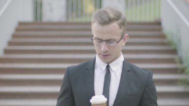 Bir fincan kahve ile merdivenlerin önünde duran gözlük yakışıklı genç iyi giyimli işadamı portresi. Ofis müdürü dışarıda ortağı bekliyor. Ofis yaşam tarzı, iş konsepti.