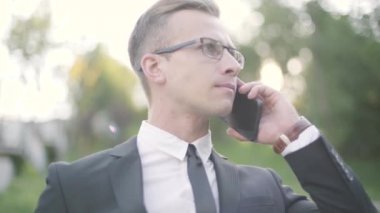 Başarılı kendine güvenen genç işadamının resmi bir takım elbise içinde portresi ciddi akıllı telefon ile ortağı veya iş arkadaşı ile konuşuyor. İş kavramı, serbest.