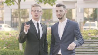 Resmi takım elbiseli iki çekici ve kendine güvenen genç işadamı sokakta başarılı bir anlaşma yaptı