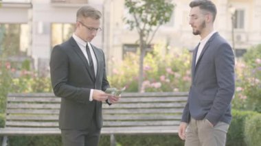 Resmi takım elbiseli iki çekici ve kendine güvenen genç işadamı başarılı bir anlaşma yaptı ve sokakta para verdi