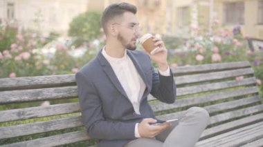 Dışarıda bir bankta oturan kendine güvenen genç işadamıportresi. Akıllı telefonuna bakıp mesaj yazıyor. Klasik giyimli. Başarılı, kendinden emin görünüyor.