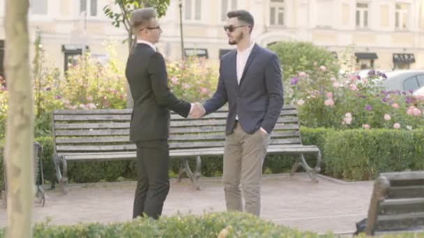 Deux jeunes hommes d'affaires se rencontrent dans le parc et se serrent la main. Gestionnaire confiant rencontre son client à l'extérieur. Réunion d'affaires, relation d'affaires — Video