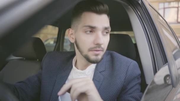 Portrait of attractive and confident young businessman in an official suit sitting in his car and going to drive. — Stock Video