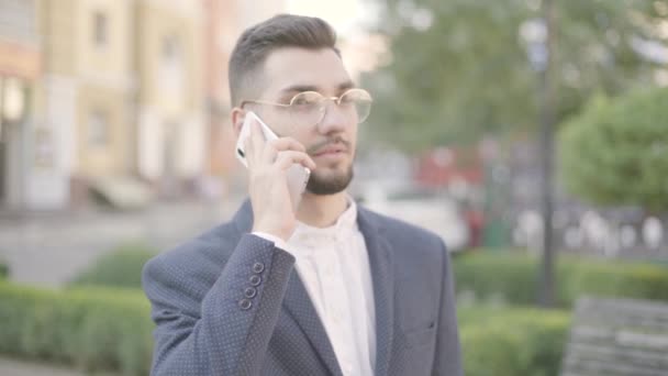 Retrato de joven hombre de negocios guapo y confiado en un traje oficial hablando seriamente con su pareja o colega por teléfono inteligente. Concepto de negocio, freelance . — Vídeo de stock