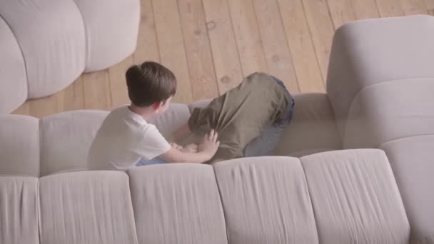 Two cute brothers laughing and fighting with each other on the sofa. Siblings spending time at home. Kids fooling around indoors. Happy family, carefree childhood. Top view — Stock Video