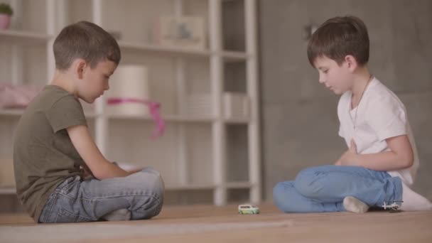 Deux petits frères assis sur le sol jouant avec la voiture jouet assis sur le sol à la maison. Les frères et sœurs passent du temps à la maison. Famille heureuse, enfance insouciante . — Video