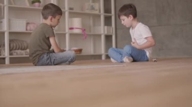 Evde yerde oturan oyuncak araba ile oynarken yerde oturan iki kardeş. Kardeşler evde vakit geçiriyorlar. Mutlu aile, kaygısız çocukluk.