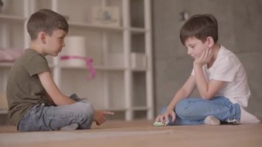 Evde yerde oturan oyuncak araba ile oynarken iki sevimli kardeşler. Kardeşler evde vakit geçiriyorlar. Mutlu aile, kaygısız çocukluk.