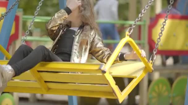 Attraente ragazza che oscilla sull'altalena nel parco giochi. Bambino felice che gioca da solo all'aperto. infanzia spensierata — Video Stock
