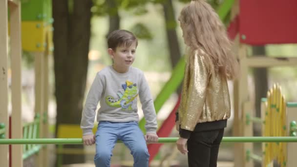 Irmãozinho e irmã mais velha brincando e conversando no playground. Relação de irmãos. A rapariga a discutir com o rapaz. Infância despreocupada. Duas crianças juntas ao ar livre — Vídeo de Stock