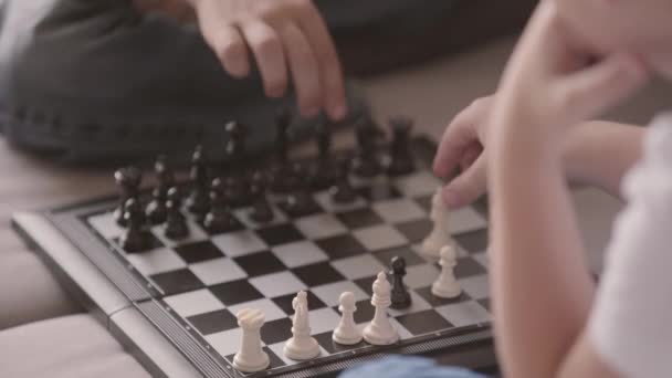 Close-up of two kids playing chess sitting on the couch. Siblings spending time at home. Happy family, carefree childhood. Intelligent game — Stock Video