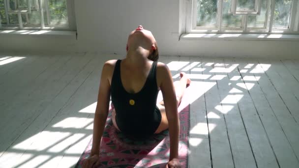 Hermosa mujer caucásica de pie sobre la alfombra en la gran sala blanca practicando yoga en el interior. Mujer joven haciendo ejercicio en la alfombra de fitness en la sala de estar . — Vídeos de Stock