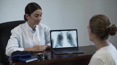 Profesyonel kadın doktor kadın hastaya bir şey söyler ve akciğer x-ray görüntü ile dizüstü ekranda gösteren. Kadınlar el sıkışır ve doktor dizüstü bilgisayarı kapatır. Meslek kavramı, tıp