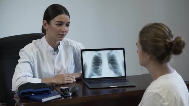 Szakmai női orvos mond valamit a női beteg, és bemutatja a képernyőn a laptop a tüdő röntgen kép. A szakma fogalma, orvostudomány, egészségügy. — Stock videók