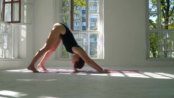 Young red-haired skills healthy caucasian woman practicing yoga on the mat in the white large room. Young woman in sports clothing exercising on fitness indoors. — Stock Video