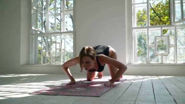 Young red-haired healthy caucasian woman practicing yoga on the mat in the white large room. Young woman in sports clothing exercising on fitness indoors. — Stock Video