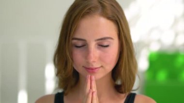 Yoga yapan oldukça konsantre beyaz bir kadının portresi. Kız yavaş yavaş derin nefes alarak el kaldırarak ve namaste jest yapıyor. Ruhsal gelişim