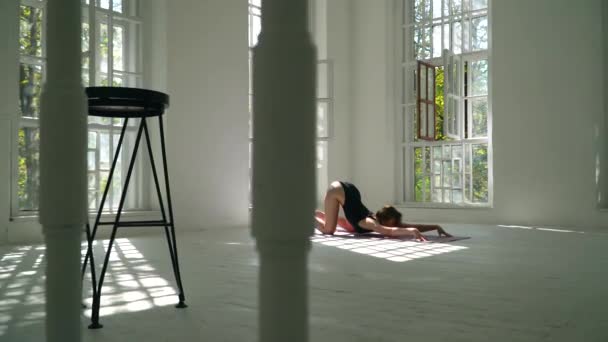 Mujer caucásica sana de pelo rojo bonita que practica yoga en la estera en la habitación grande blanca. Mujer joven en ropa deportiva haciendo ejercicio en el gimnasio en el interior . — Vídeo de stock