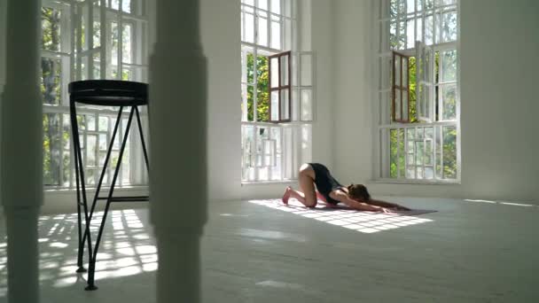 Joven mujer caucásica sana pelirroja practicando yoga en la esterilla en la habitación grande blanca. Mujer joven en ropa deportiva haciendo ejercicio en el gimnasio en el interior . — Vídeo de stock